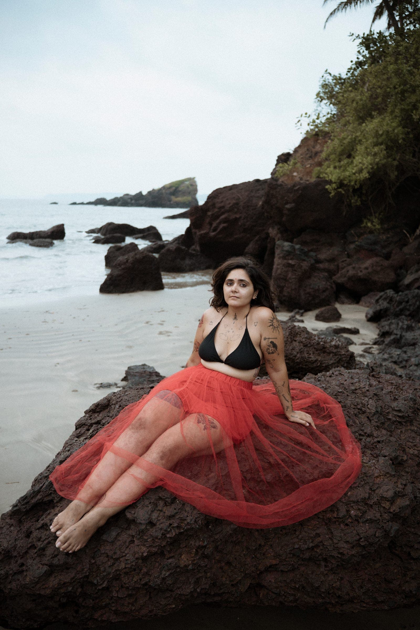Hansika seated on coastal rocks in a red skirt